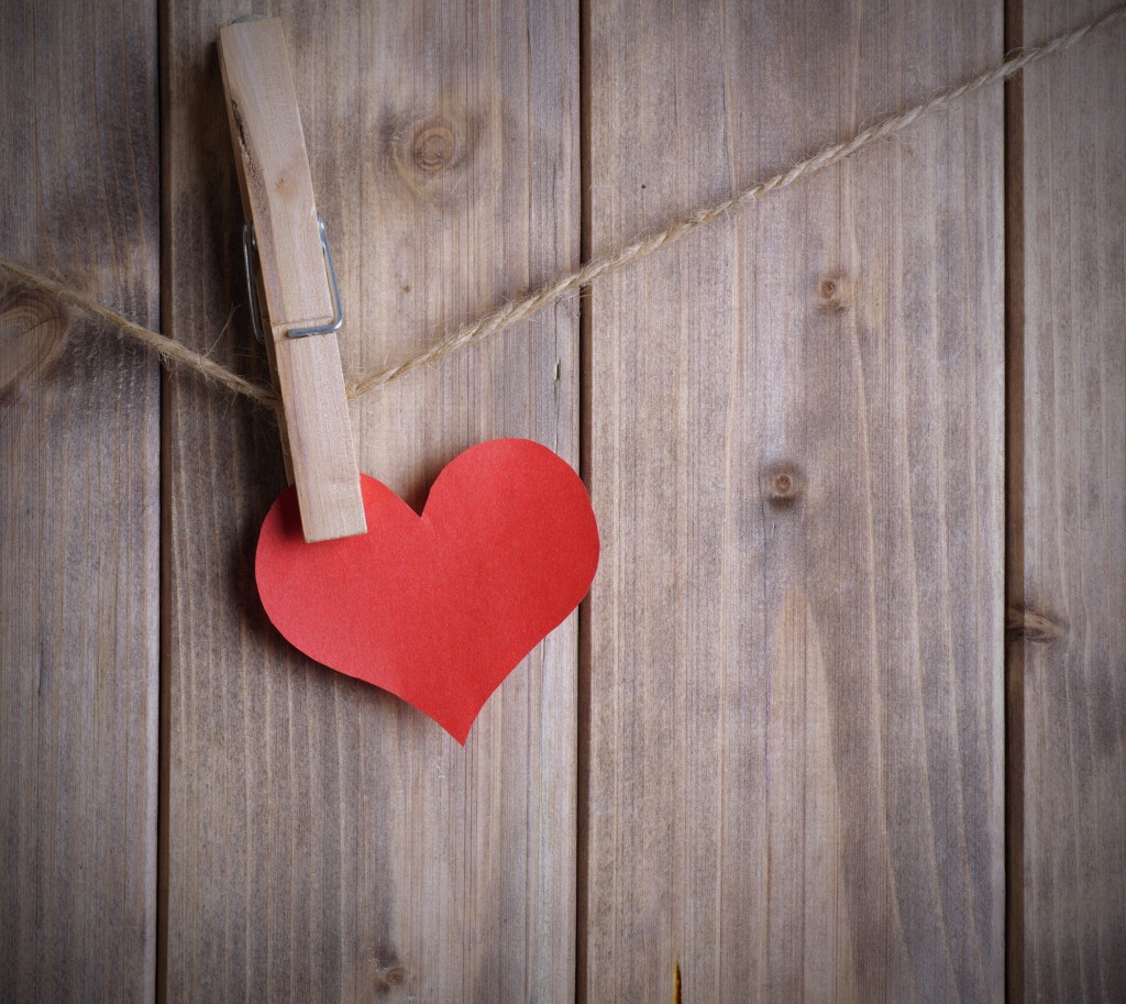 red heart made of paper with clothespin hanging on a rope and wooden planks background with space for text